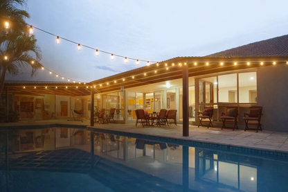 patio string bulbs glowing warm over backyard pool at dusk